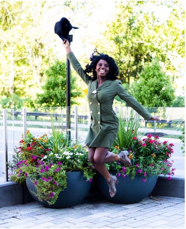 VOA jumping with her hat lifted in the air with flower and trees as background